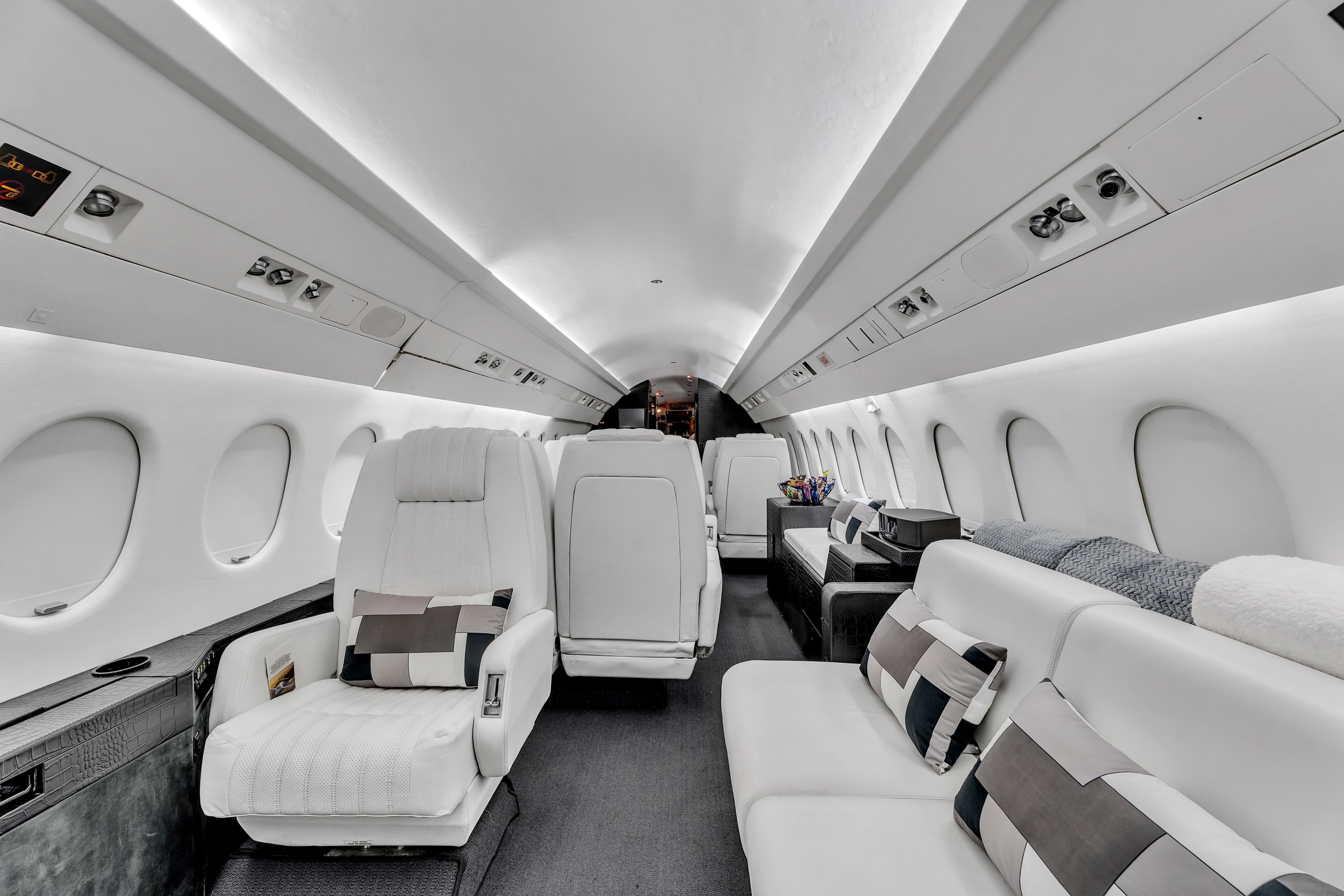 Falcon 900 cabin with white leather armchairs, a long divan, and dark textured cabinetry